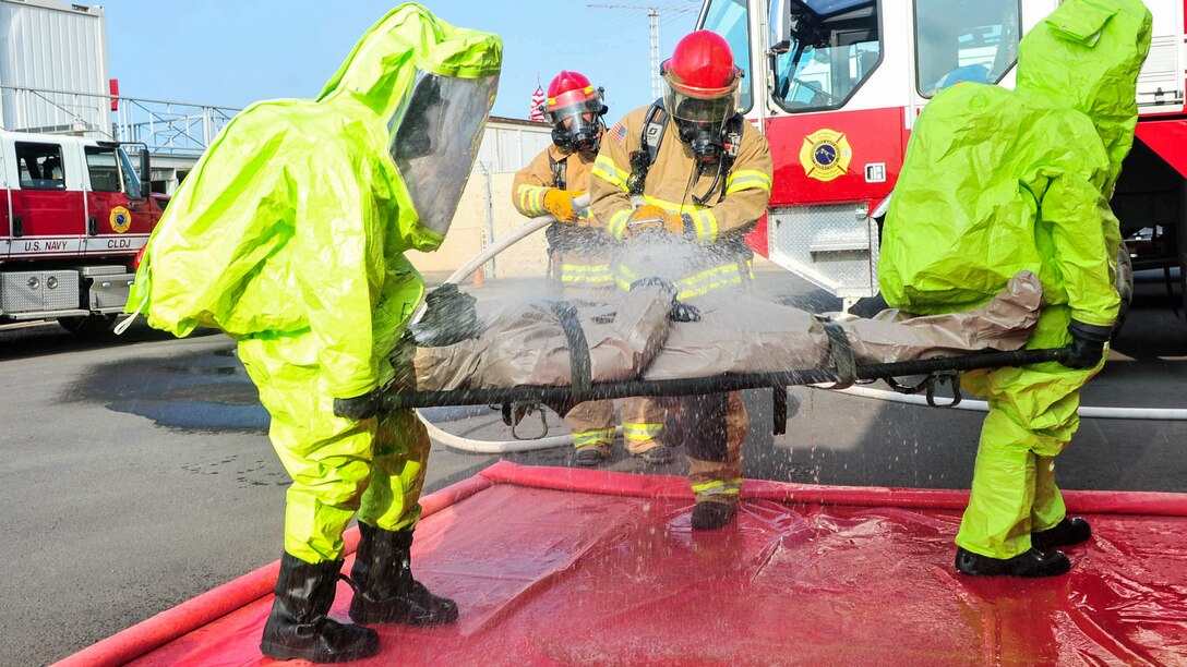 Firefighters and sailors in green protective suits participate in a hazardous material exercise.