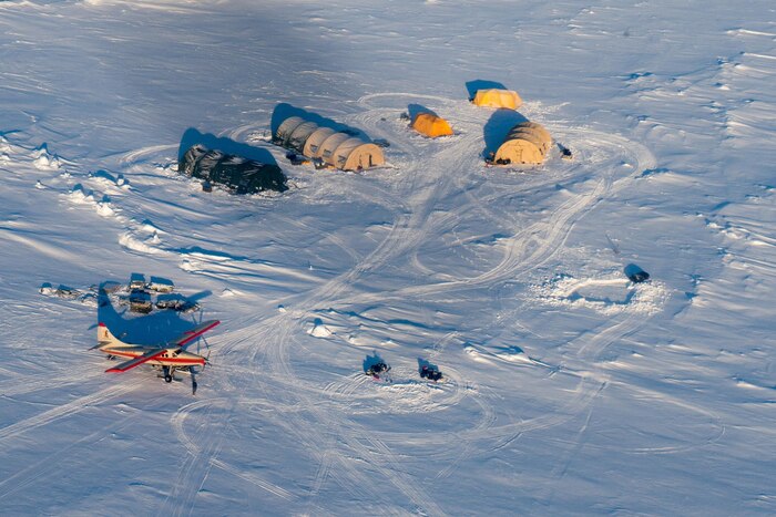 Shelters and an aircraft sit on the ground.