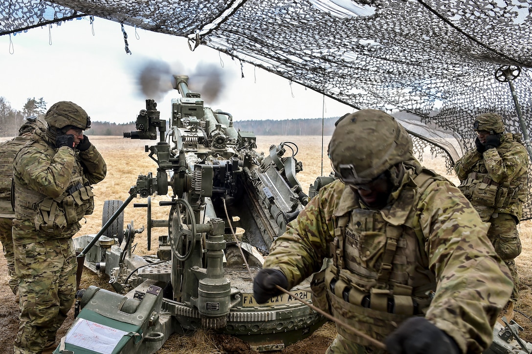 Soldiers under a cover fire an M777 howitzer during a field exercise.