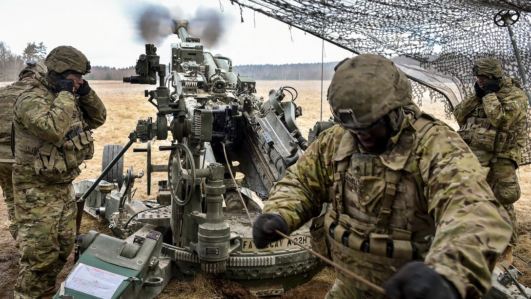 Soldiers under a cover fire an M777 howitzer during a field exercise.