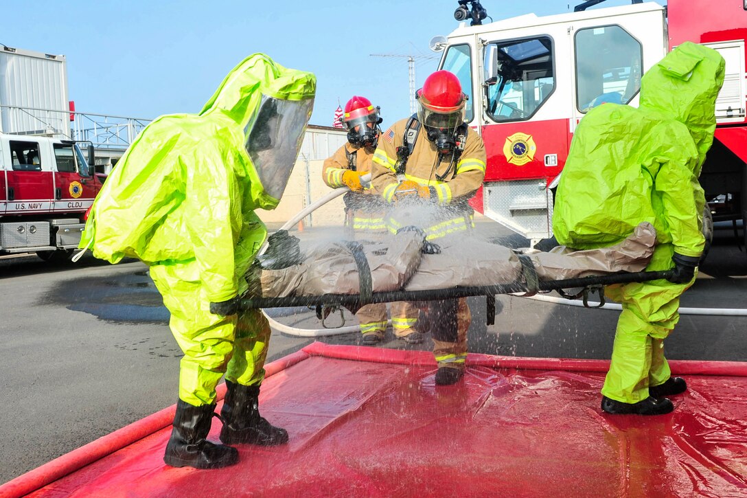 Firefighters and sailors in green protective suits participate in a hazardous material exercise.