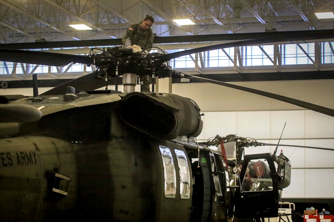 A soldier performs maintenance on the main rotor blades of a helicopter.