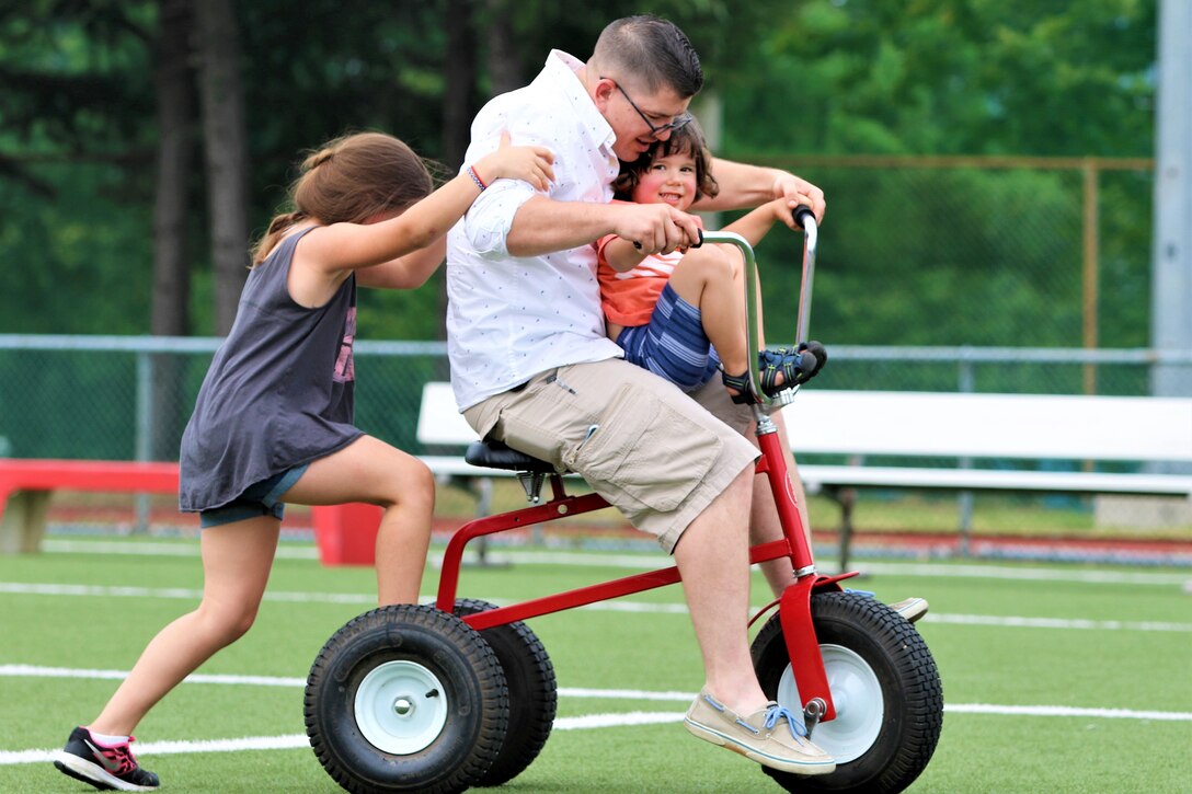 An adult rides on an oversize trike with two children.