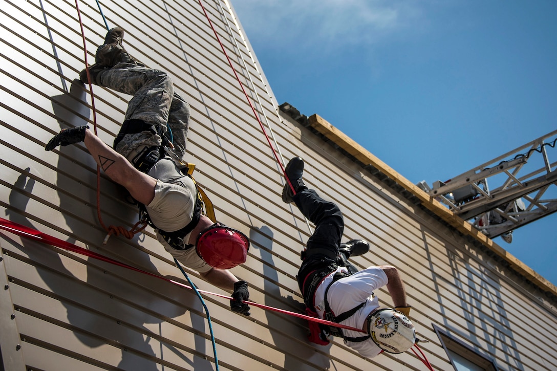 Two rappellers hang on a building side and grasp a ribbon on the building.