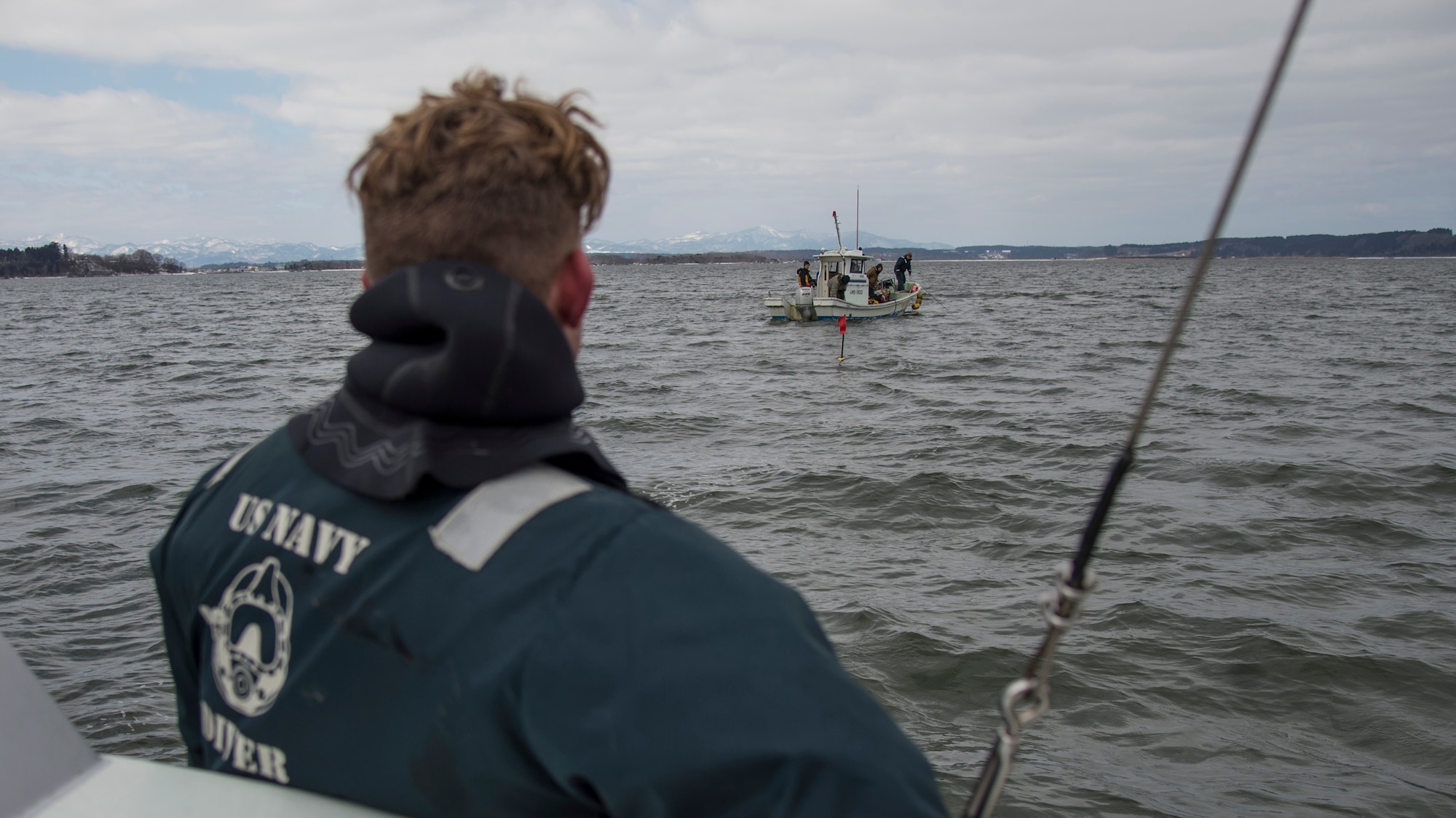 U.S. Navy Diver 2nd Class Mitchell Apgar, assigned to Commander, Fleet Activities Sasebo, watches another boat conduct cleanup efforts at Lake Ogawara, Tohoku Town, Japan, March 10, 2018.