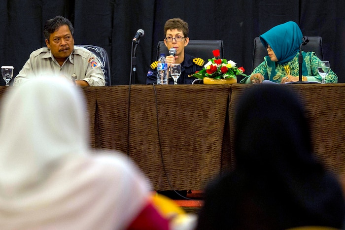 Three people at a table speak to an audience.