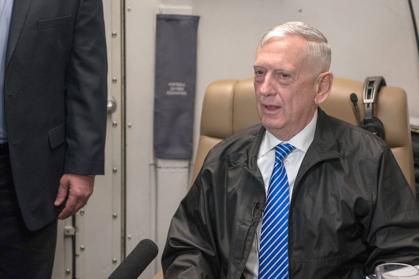 Defense Secretary James N. Mattis sits in an aircraft seat and talks.