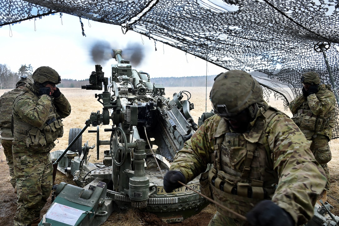 A soldier pulls the lanyard firing a M777 howitzer.
