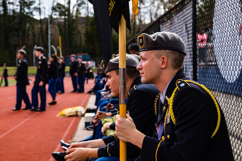 A guidon bearer watches his classmates compete in an unarmed platoon exhibition during the North Springs Charter High School Invitational Drill Meet. U.S. Army Soldiers from the 335th Signal Command (Theater), and Georgia Recruiting Battalion, U.S. Army Recruiting Command served as judges and mentors for  Georgia area Junior Reserve Officer Training Corps (JROTC) students from 13 high schools at the North Springs Charter High School Invitational Drill Meet held in Atlanta, Feb. 24, 2018. (U.S. Army photos by Capt. David Gasperson).