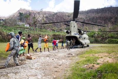 Army Sgt. Delton Reynolds, left, a flight engineer with Joint Task Force Leeward Islands, joins a chain with local residents and members of the Jamaican defense force to unload relief supplies from a CH-47 Chinook helicopter at Wotten Waven, Dominica.