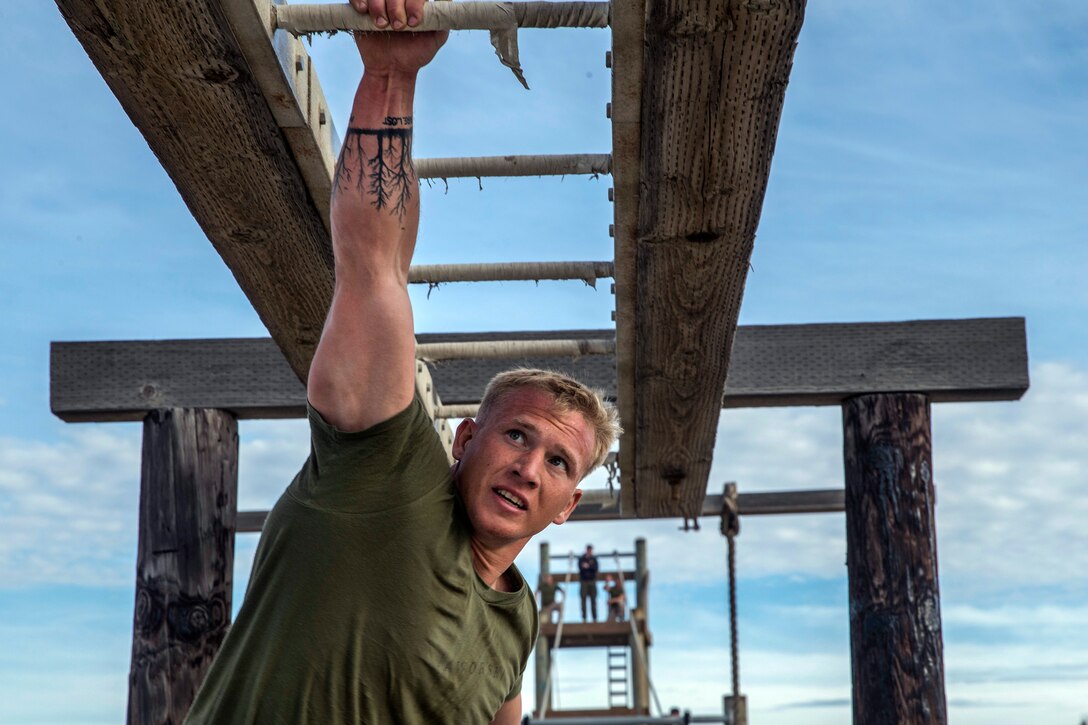 A sailor hangs from one arm on a bar obstacle.