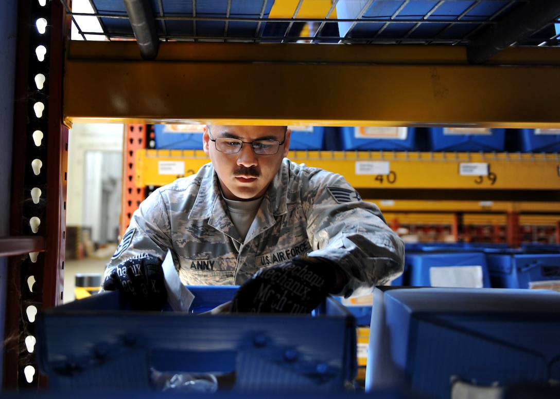 A male leans on blue containers with parts in a warehouse.