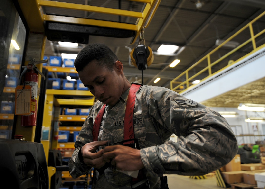 A male puts on a red harness in a warehouse.