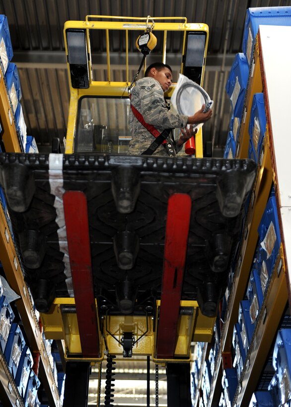 A male stands on a yellow forklift in a warehouse high in the air.