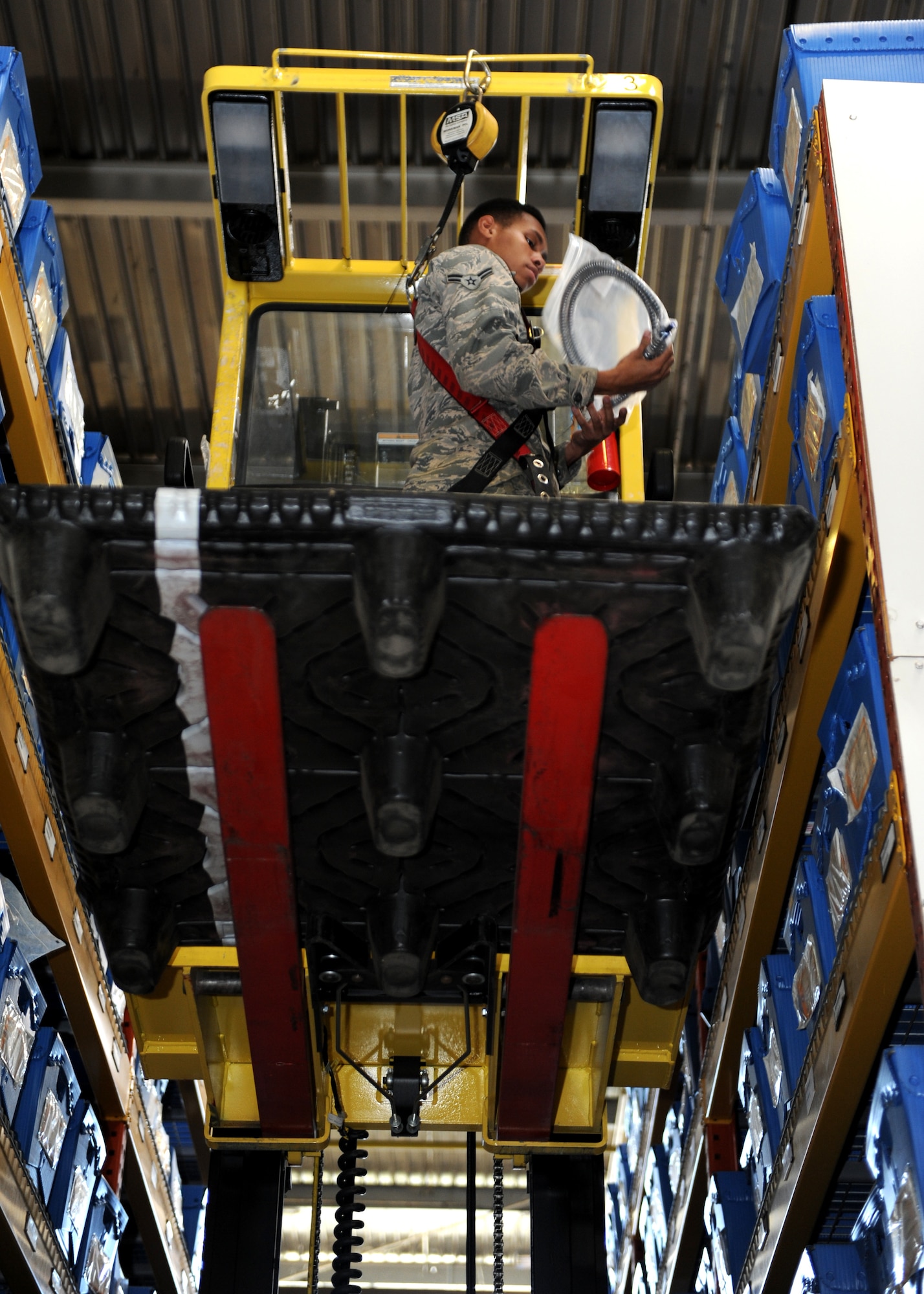 A male stands on a yellow forklift in a warehouse high in the air.