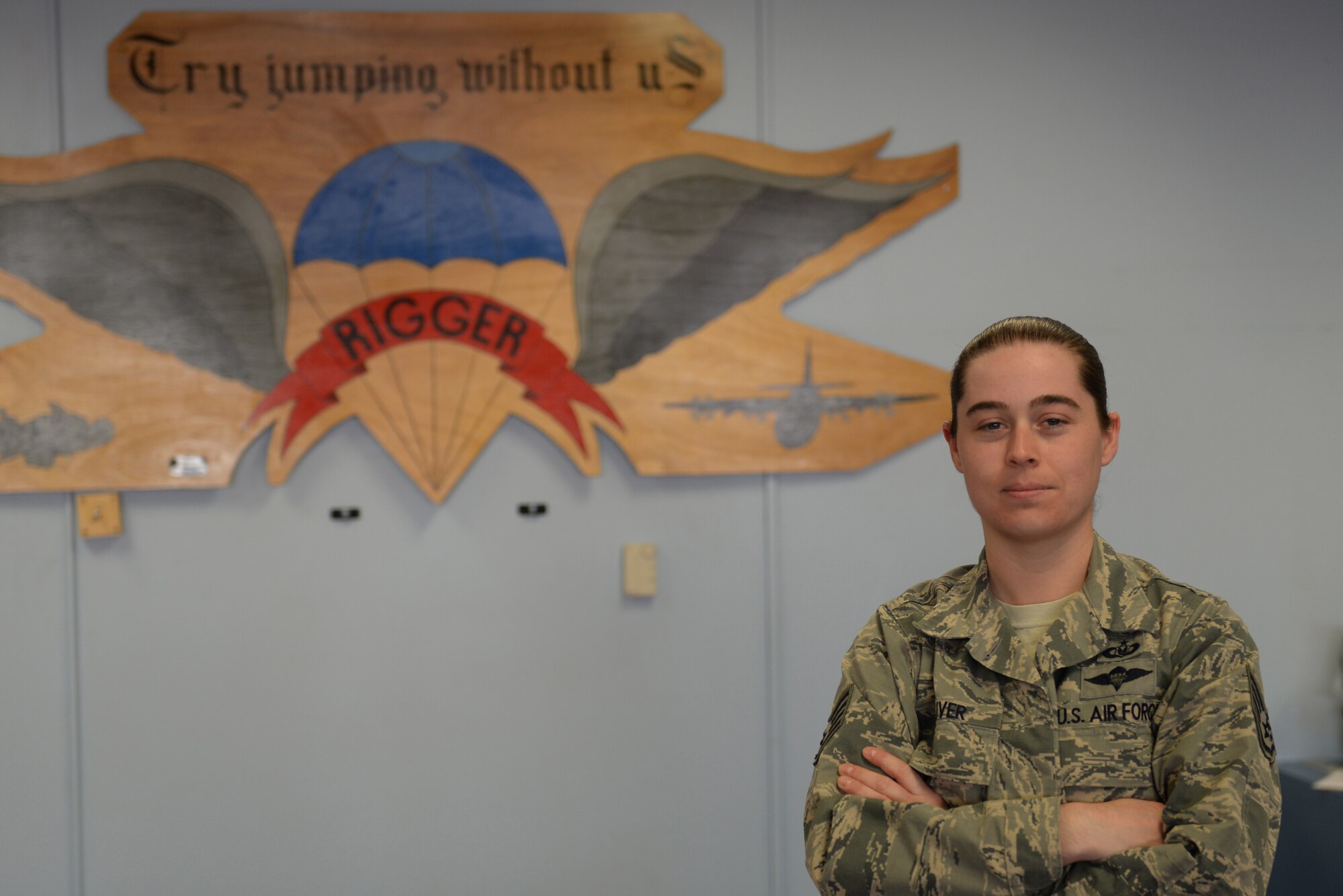 Woman in the Airman Battle Uniform stands with her arms folded in front of a parachute sign.