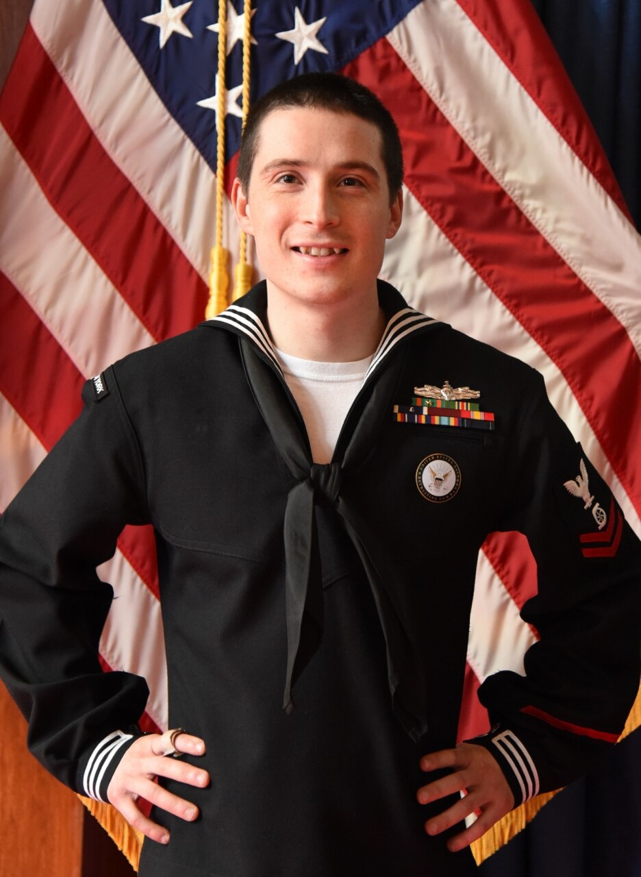A Navy Chief Petty Officer stands in front of American flags.