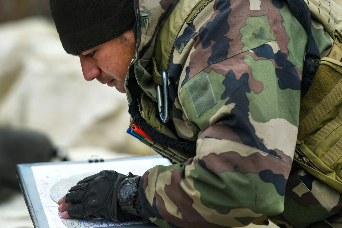 A French soldier plots coordinates on a terrain map.