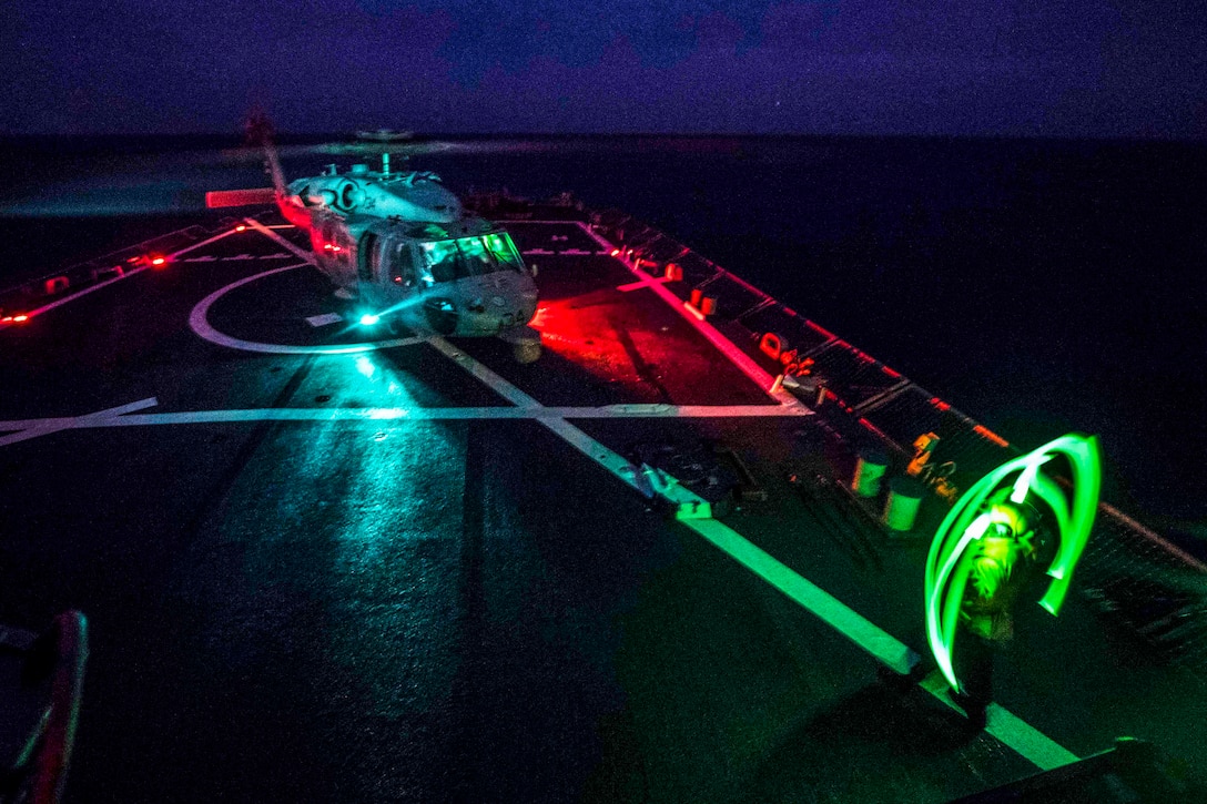 A sailor signals to a helicopter on a ship at night.