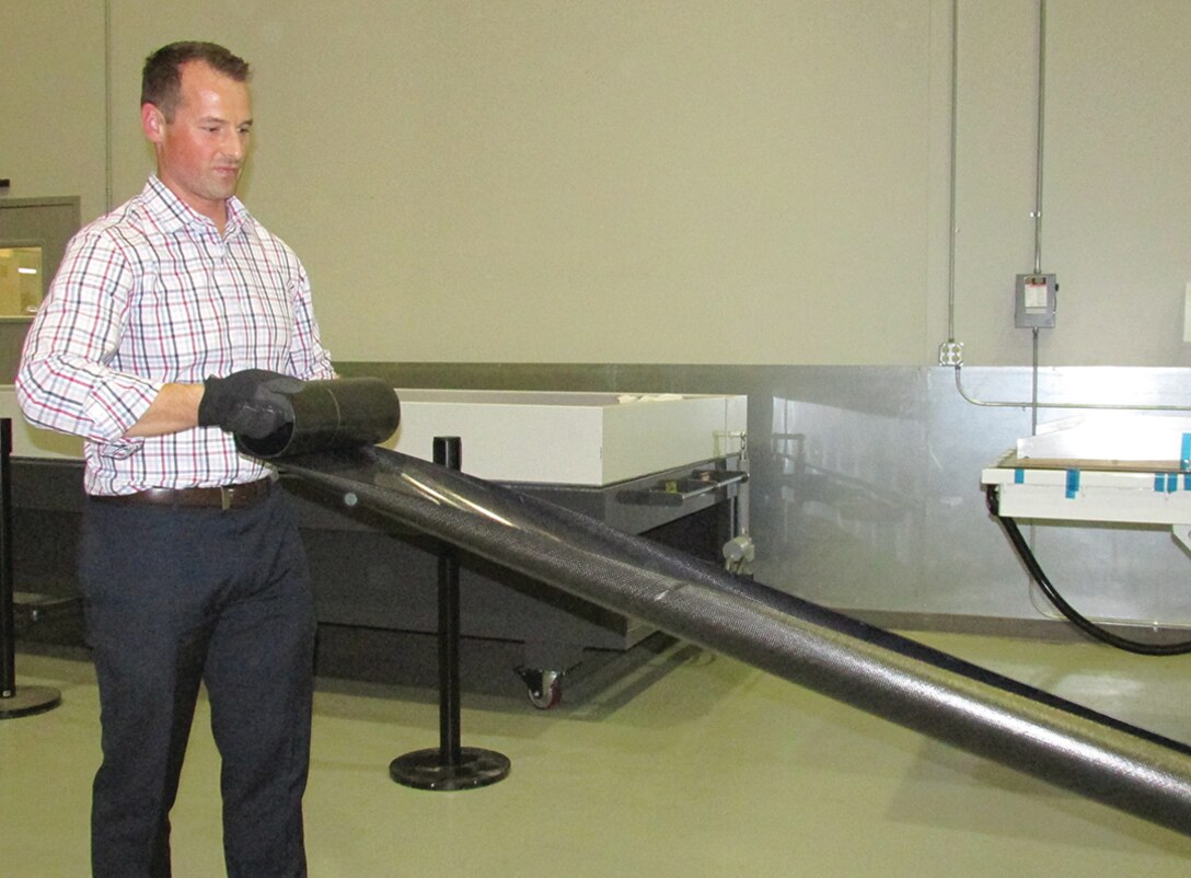 Jeremy Banik, Air Force Research Laboratory Space Vehicles Directorate's principal investigator on the Roll-Out Solar Array program, shows the AFRL-developed boom for the solar array. The boom is 16 feet long, and rolls out and back up using strain energy.