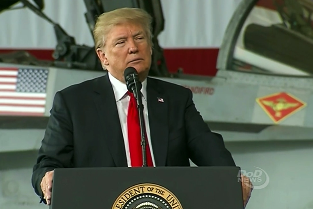 President Donald J. Trump speaks at a lectern in front of an aircraft.