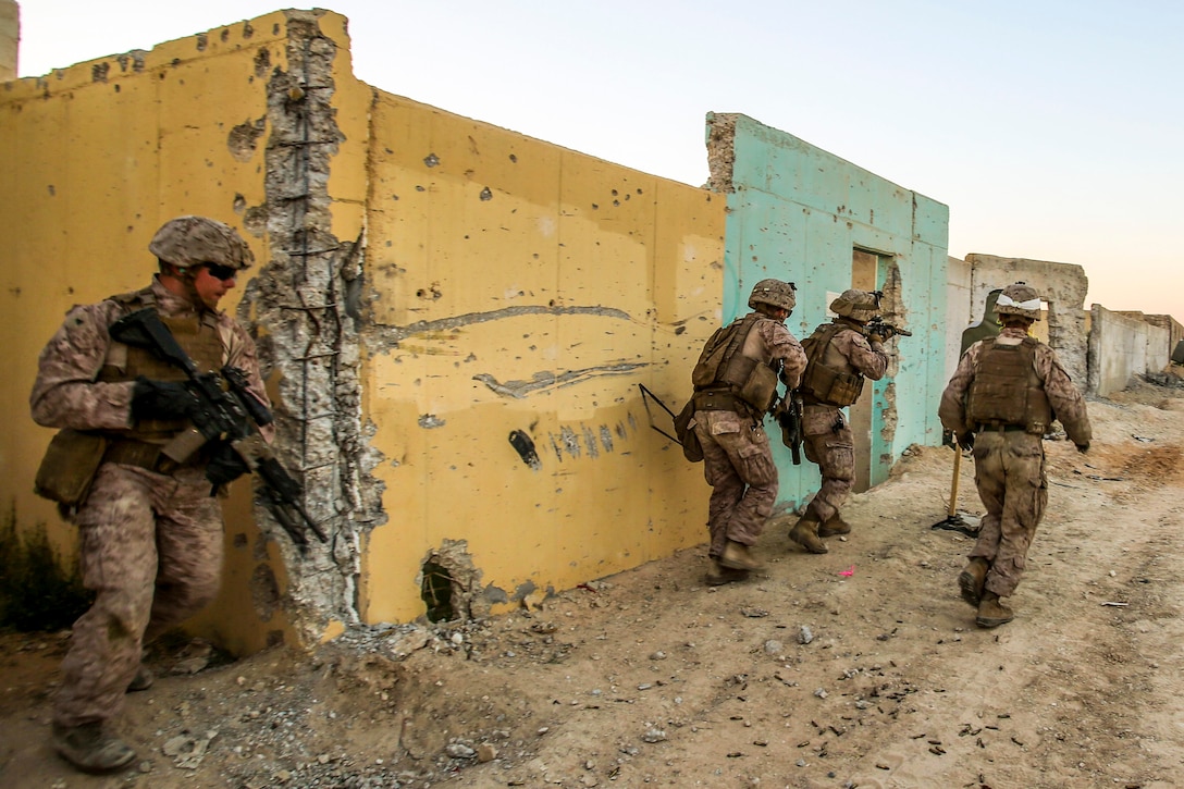 Marines conduct a live-fire exercise next to yellow and turquoise building during an exercise in Israel.