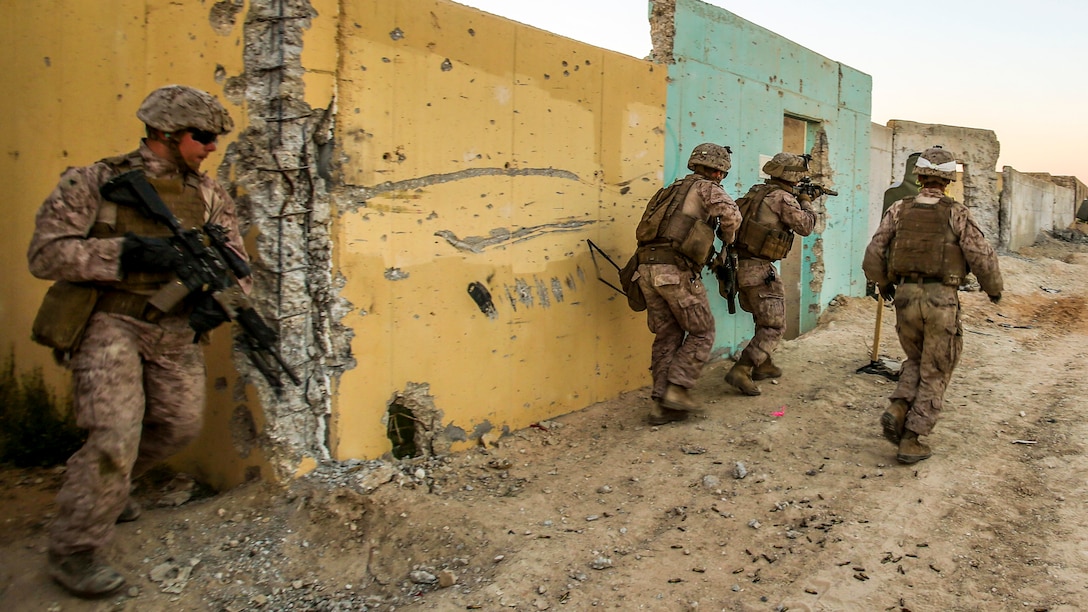 Marines conduct a live-fire exercise next to yellow and turquoise building during an exercise in Israel.