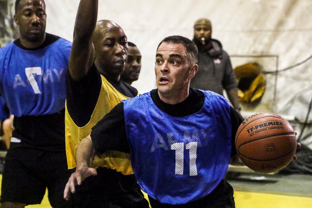 A soldiers holds a basketball in one hand as he contemplates his next move during a game.