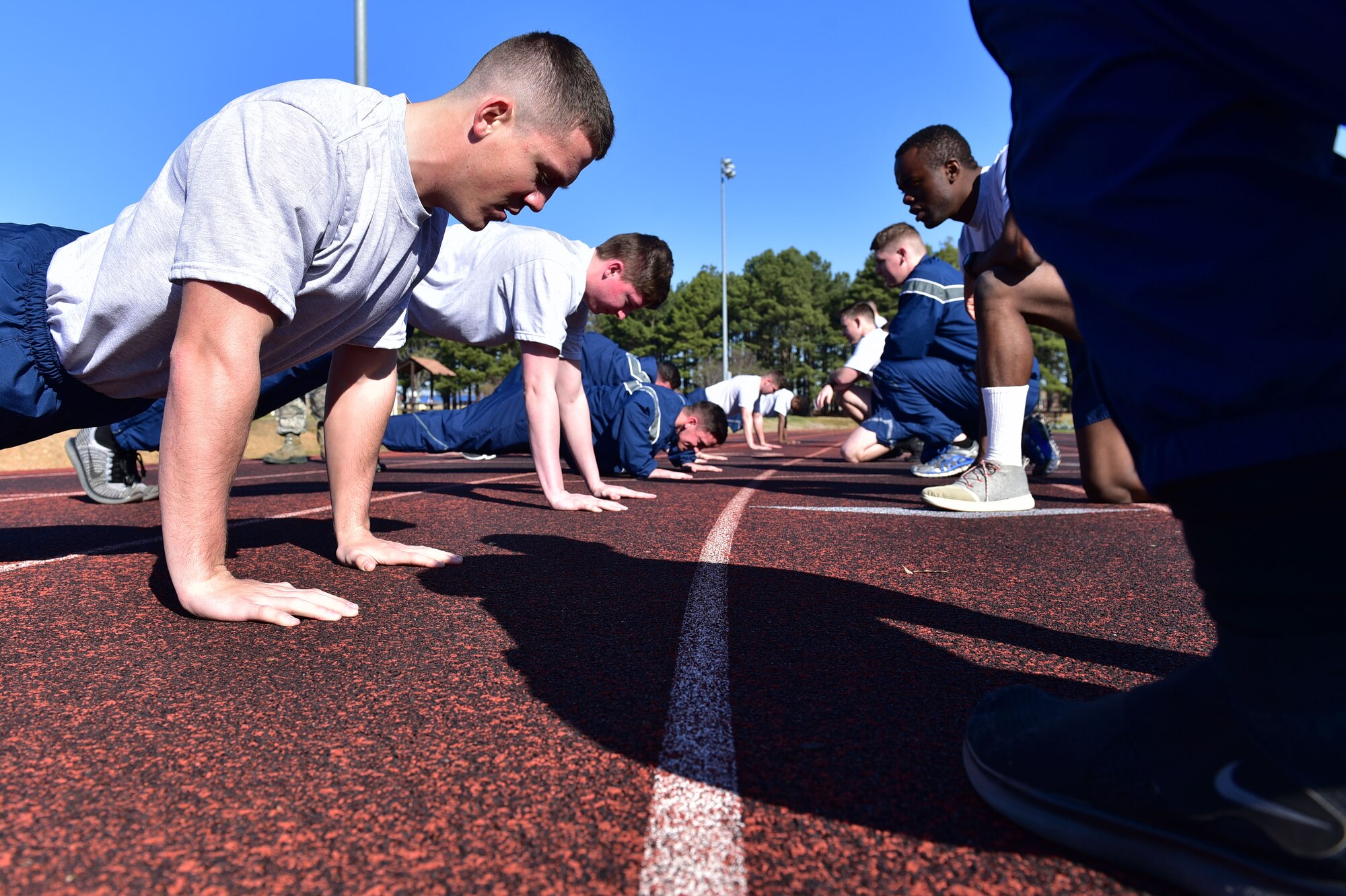 Airmen do push-ups, while other Airmen kneel in front of them.