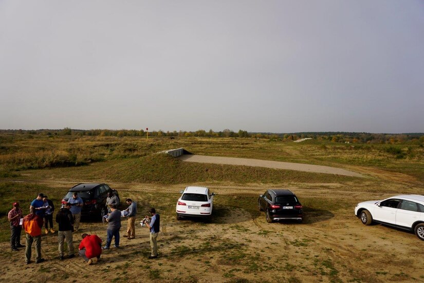 A group of people stand together in a field, examining documents.