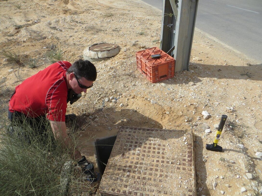 A man crouches on the ground and inspects a manhole cover.