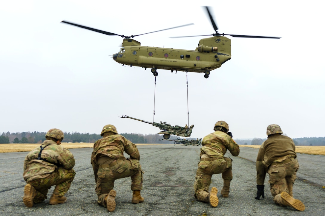 Soldiers observe as a CH-47 Chinook helicopter takes off.