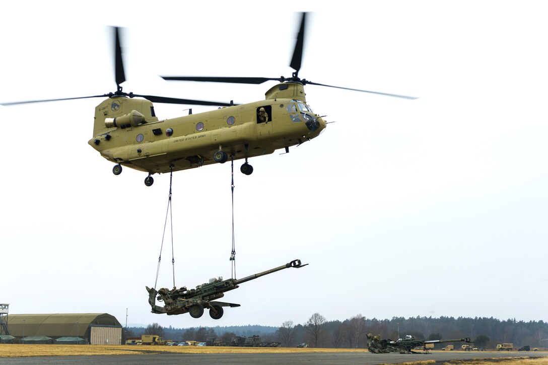 A CH-47 Chinook helicopter lifts off slingloading an M777 howitzer.