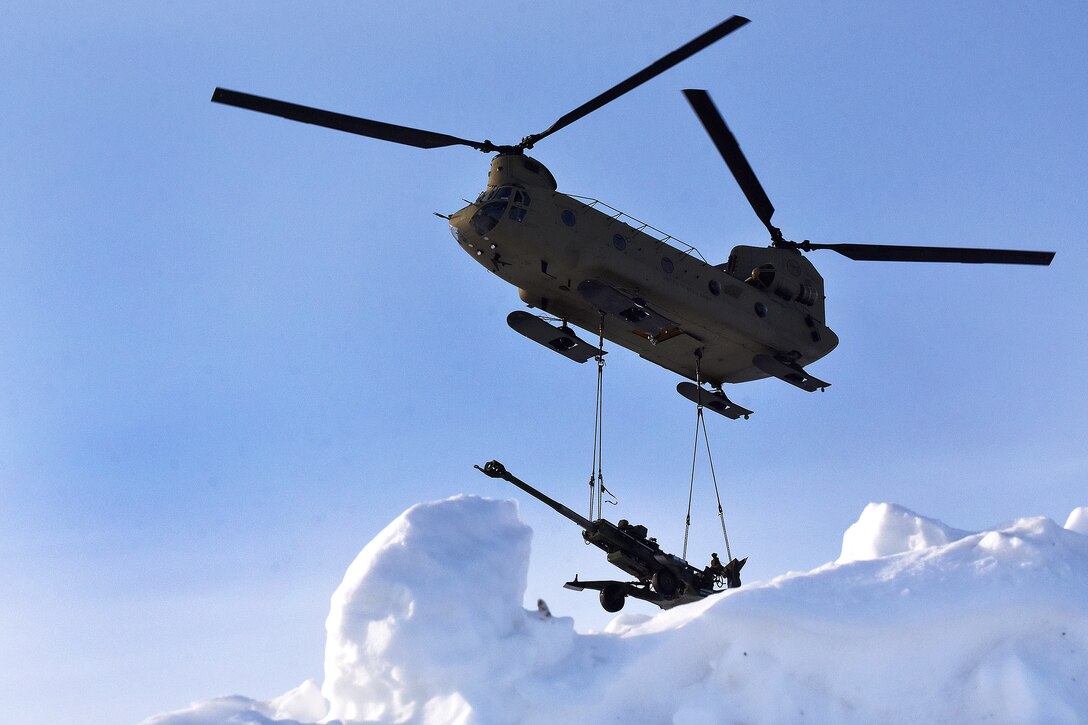 A CH-47 Chinook helicopter sling-loads a 155 mm howitzer.