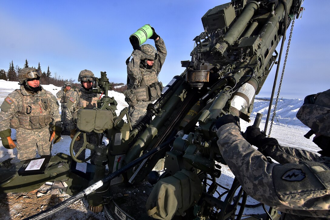 Soldiers load a round into a 155 mm howitzer.