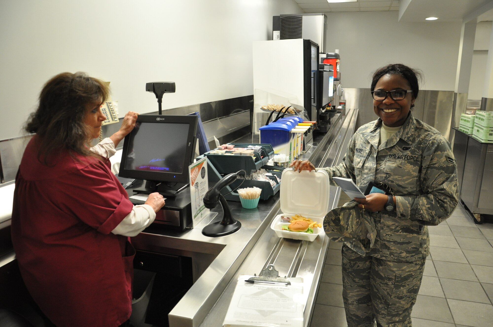 Nancy McCloud, Pitsenbarger Dining Facility cashier, rings up Airman 1st Class Tavia Moore’s short order food total at the Pitsenbarger Dining Facility, located in Building 1214, Area A, Kittyhawk. (U.S. Air Force photo/W. Eugene Barnett Jr.)