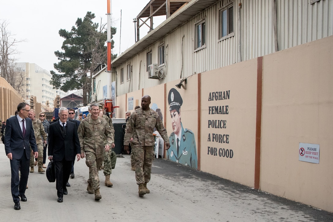 Defense Secretary James N. Mattis walks down a street with service members.