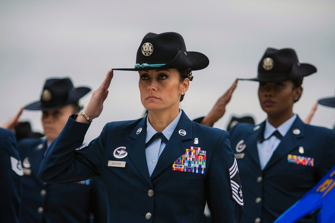 Female military instructors stand in formation and salute.