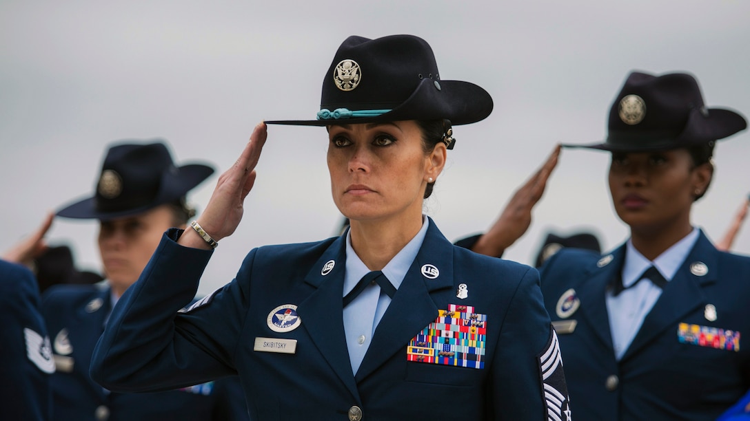 Female military instructors stand in formation and salute.