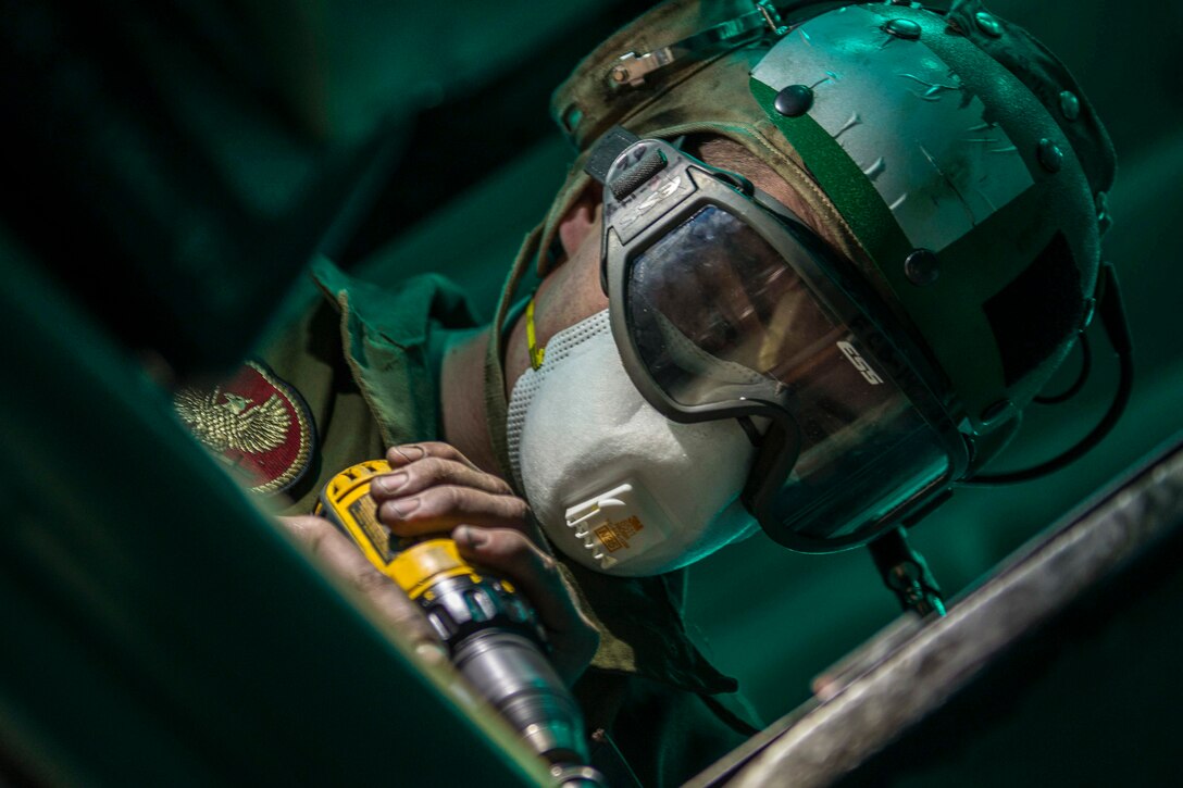 A Marine wearing protective goggles tilts his head and uses a tool to perform maintenance.