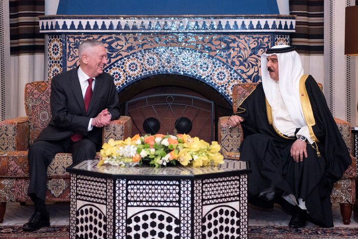 Defense Secretary James N. Mattis and the Bahraini king smile and chat while sitting in armchairs in front of an ornate tiled fireplace.