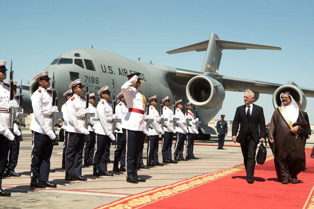 Troops salute Defense Secretary James N. Mattis and his Bahraini counterpart as they walk on a red carpet on a flightline.