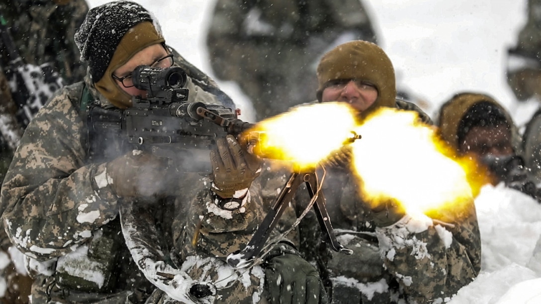 A soldier fires a machine gun with a blank firing adaptor during an exercise in the snow.