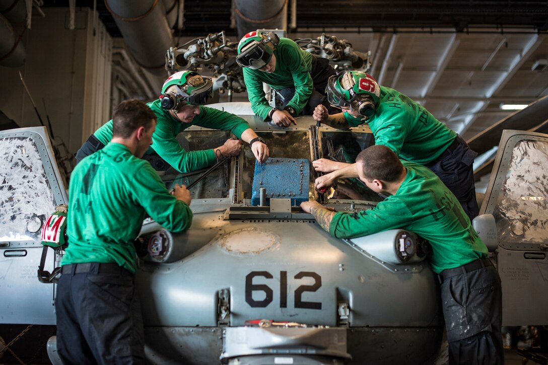 Sailors in green tops replace a windshielf on a helicopter on a ship.