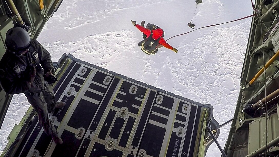 Airmen parachute from an aircraft on to a frozen sea.