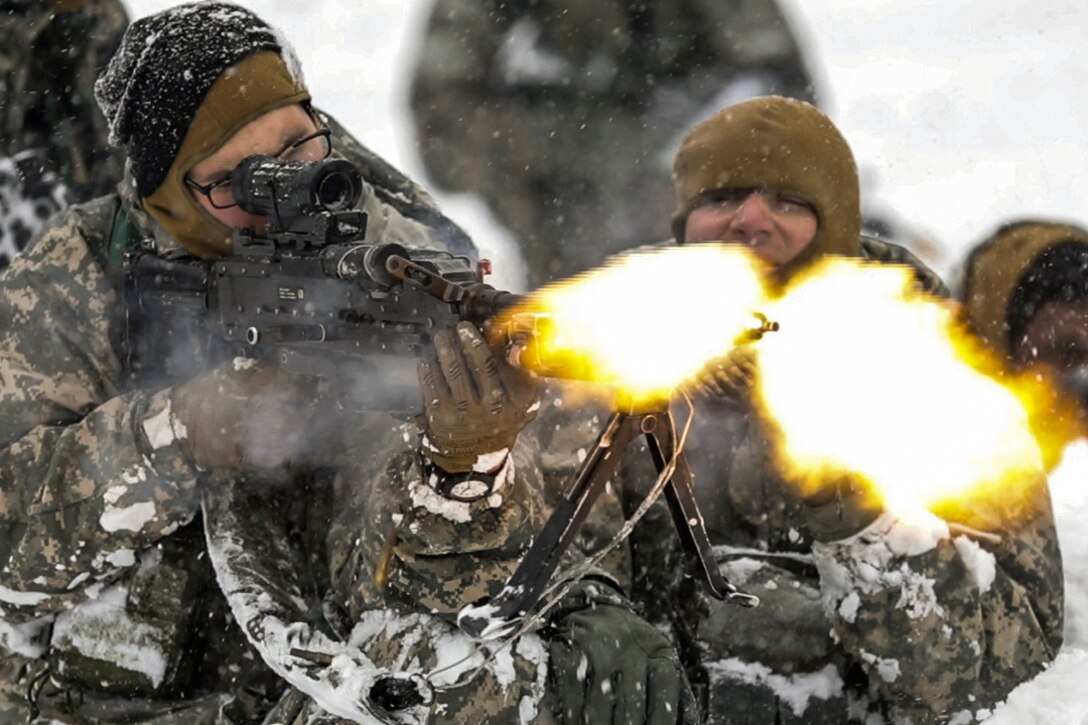 A soldier fires a machine gun with a blank firing adaptor during an exercise in the snow.