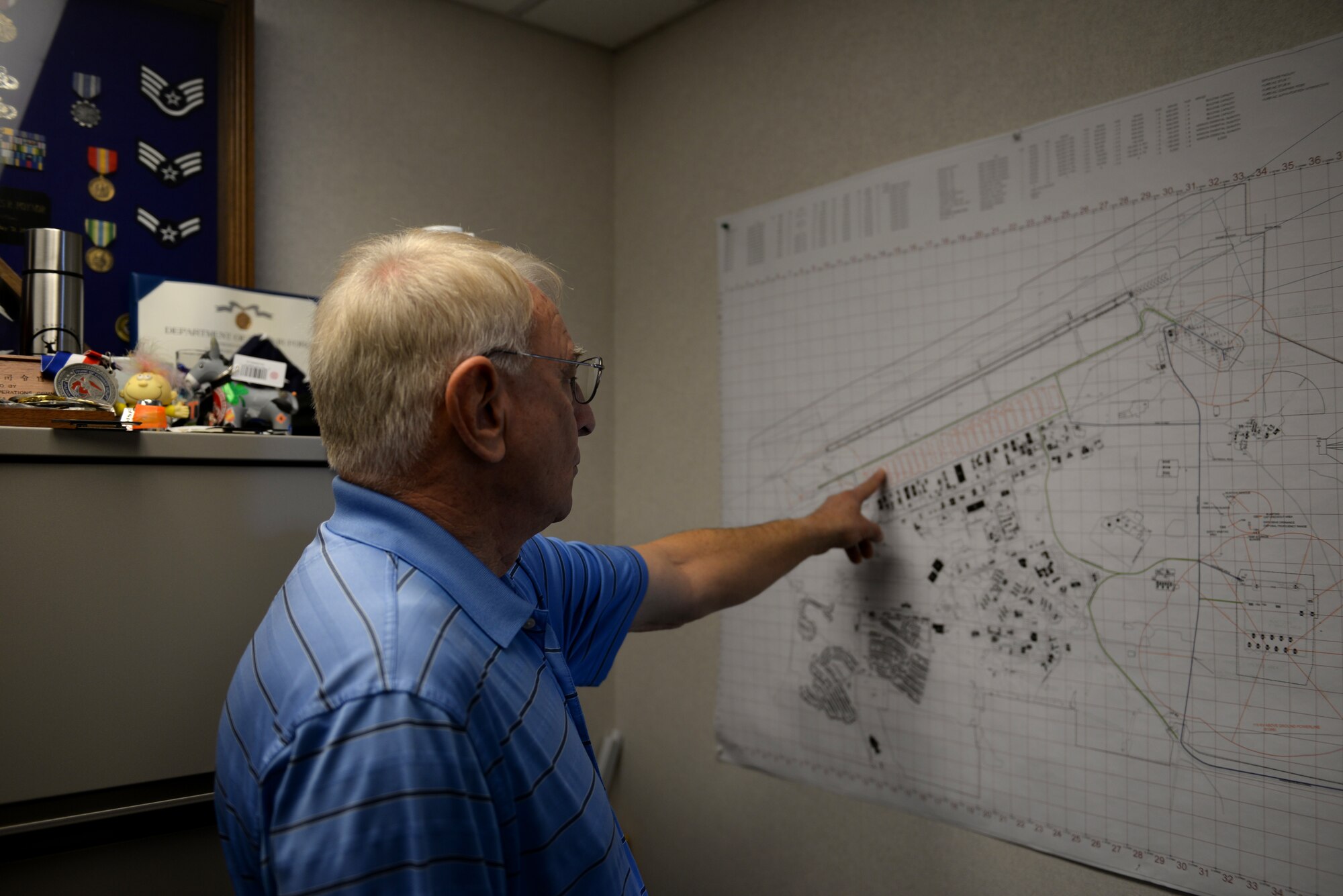 Man wearing a blue striped polo shirt points to a map.