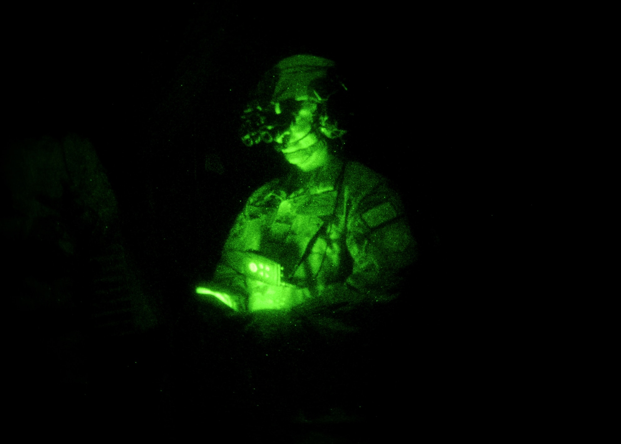 A green night vision photo depicting a male wearing night vision goggles in a completely black aircraft.