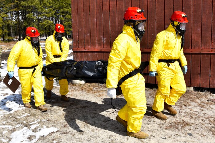 Service members in yellow suits carry a simulated casualty on a stretcher.