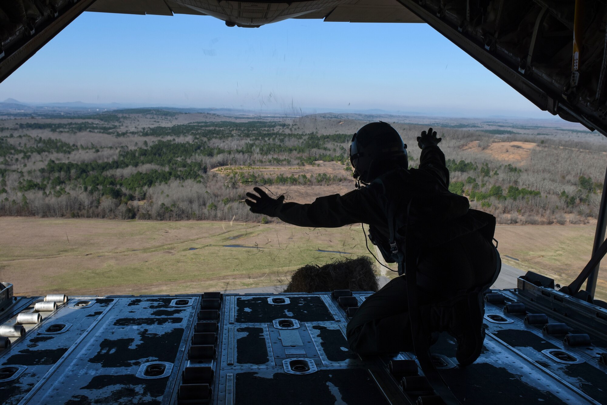 An Airman flies in the back of an aircraft and drops a hay bale during a training event